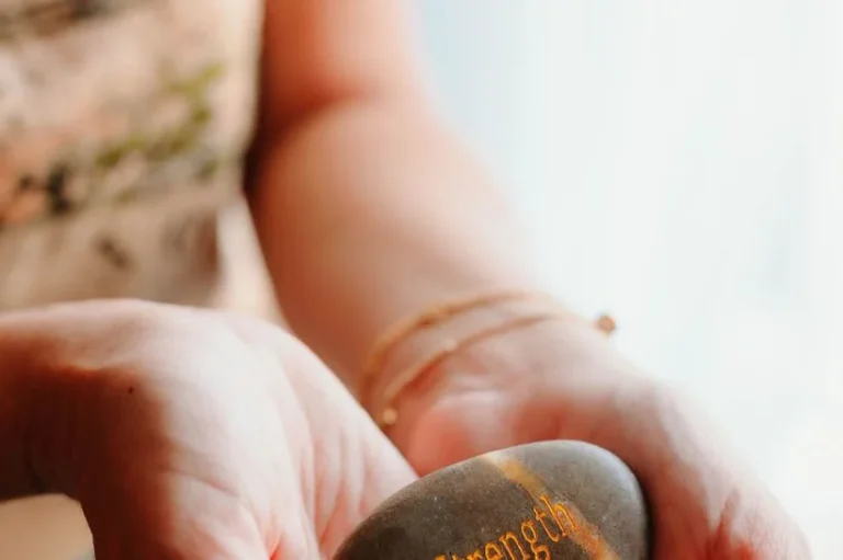 A hand holding a stone engraved with the word strength